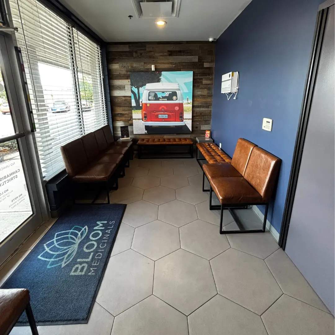 Bloom west columbus dispensary waiting room with brown leather chairs, a hexagonal-tiled floor, and a colorful van painting on a wooden-panel wall.