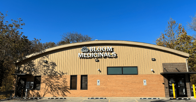A single-story building with a sign reading "Bloom Medicinals" against a clear blue sky, surrounded by trees.